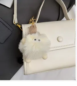 Dettaglio del ciondolo in peluche bianco con cappello marrone appeso a una borsa beige