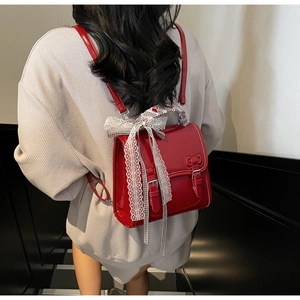 Detail of red patent leather backpack with large white lace bow and metal buckles