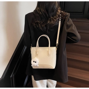 Sac à main blanc crème porté par un mannequin avec une finition texturée et un pompon
