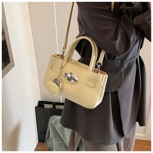 Detail of a beige pebbled leather bucket bag with silver heart charm and turn-lock closure
