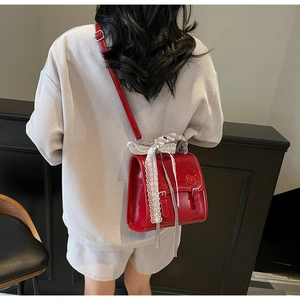Detail of red patent leather backpack with white lace bow and buckle closure on model