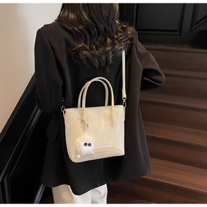 Détail du sac cabas beige marbré avec breloque peluche sur un costume noir