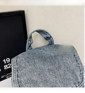 Détail de la poignée supérieure renforcée et du rabat du sac à dos en denim bleu avec coutures