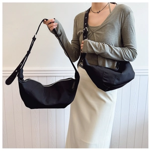 Detail of black pleated dumpling shoulder bag with metallic eyelets on the adjustable strap