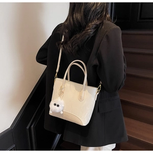 Détail d'un sac à main crème en similicuir avec logo et petit pendentif monstre en peluche