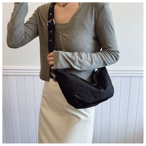 Detail of black nylon dumpling bag featuring wide shoulder strap with silver metal eyelets