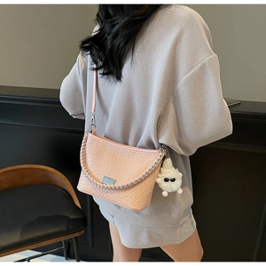 Close-up of pink woven leather shoulder bag featuring silver chain and cute plush charm