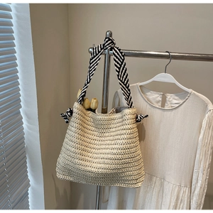 Détail d'un sac cabas en paille tressée avec anses rayées noir et blanc et nœuds