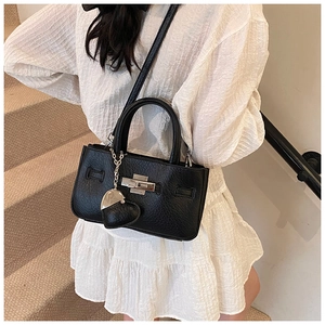 Detail of black pebbled leather handbag featuring metal twist lock and heart-shaped charm