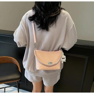 Detail of light pink woven crossbody bag with metal chain and plush monster charm