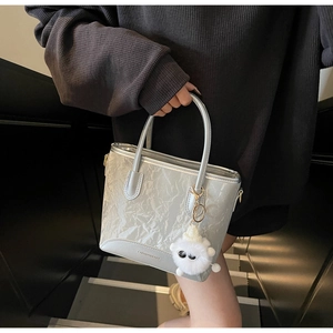 Détail du sac cabas argenté avec texture froissée et breloque en peluche blanche