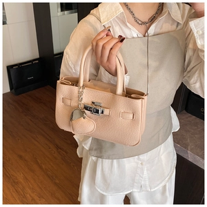 Detail view of beige textured handbag with silver buckle and heart-shaped metal pendant
