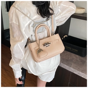 Detail of elegant beige bucket bag with heart charm and crossbody strap on model