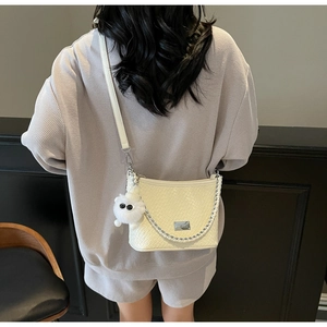 Detail view of cream underarm bag with woven texture, silver chain, and plush charm