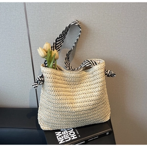 Détail d'un sac cabas en paille beige avec une bandoulière nouée à rayures noir et blanc
