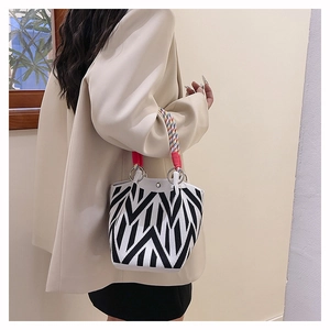 Detail van geometrische bucket bag met kleurrijk gevlochten handvat en zilveren ringen