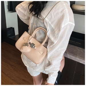 Close-up of beige leather crossbody bag with metal twist lock and heart pendant detail