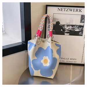 Detail van gebreide emmertas met blauwe bloemenborduurwerk en kleurrijke gevlochten handvatten