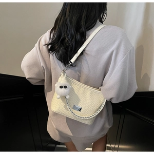 Detail view of beige woven texture bucket bag with silver chain and plush pendant