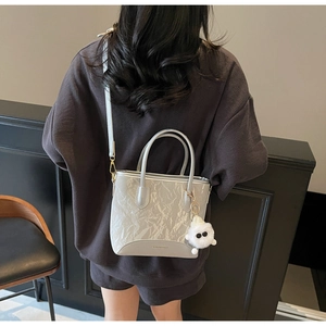 Détail d'un sac argenté plissé avec pompon décoratif et logo tendance porté par un mannequin