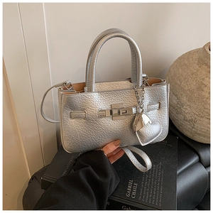 Macro view of silver metallic textured bucket bag with heart pendant and lock detail