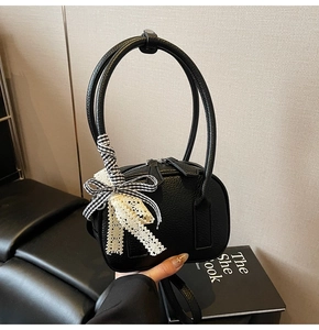 Dettaglio della mini borsa in pelle nera con fiocco in pizzo e tessuto a quadretti