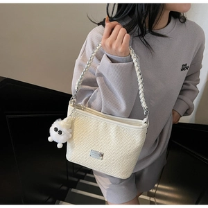 Detail of white woven underarm bag with plush ball charm and silver logo plaque