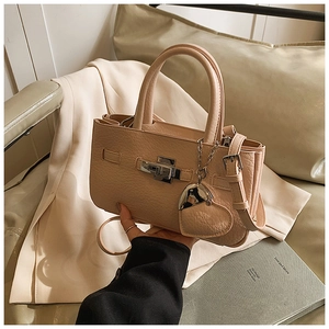 Close-up of beige lychee textured handbag with silver lock and heart charm