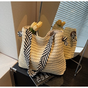 Détail d'un sac cabas en paille beige avec bandoulière rayée et accents floraux internes