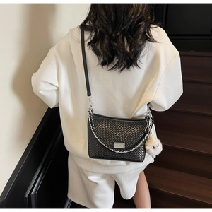Detail of black woven shoulder bag featuring silver chain and cute white plush sheep charm
