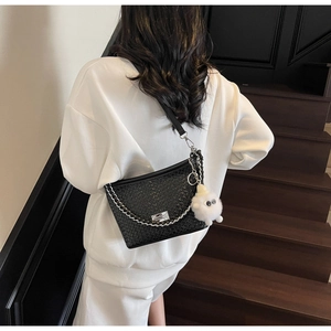 Detail of woven black shoulder bag featuring silver chain and cute white plush sheep charm