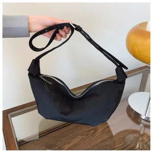 Detail of a black crescent shoulder bag with knotted strap and silver zipper closure