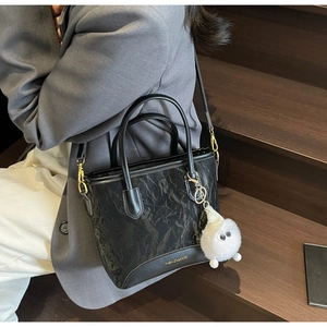 Détail de la texture cuir plissé noir et du charm de sac monstre blanc en peluche