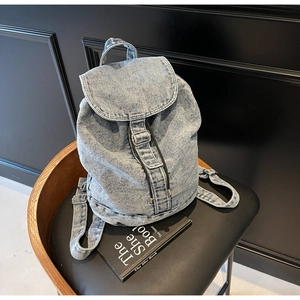 Détail du sac à dos en jean bleu clair avec cordon de serrage et boucle sur une chaise