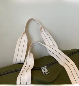Detail of army green canvas travel bag featuring durable dual metal zippers and striped strap