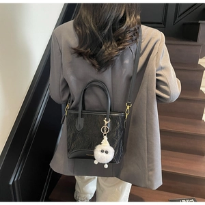 Détail du cabas noir plissé avec charm pompon blanc porté par un mannequin chic