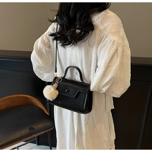Dettaglio borsa in pelle nera con patta geometrica e ciondolo di peluche bianco