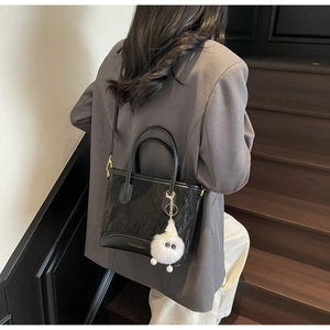 Vue détaillée d'un sac seau noir plissé avec ferrures dorées et pompon blanc décoratif
