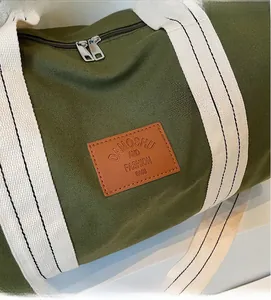 Detail of army green canvas travel bag featuring brown leather logo patch and metal zipper