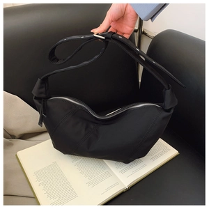 Detail of black crescent shoulder bag with diagonal stitching on a leather sofa
