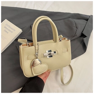 Detail of beige lychee leather crossbody bag with silver buckle and heart pendant charm