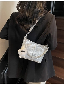 Silver woven hobo shoulder bag with chain strap and plush charm worn by model in a suit