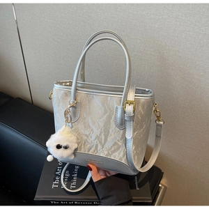 Détail d'un sac cabas argenté métallisé avec breloque en peluche sur livre noir