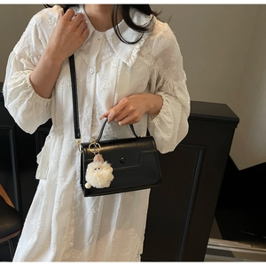 Dettaglio borsa in pelle nera con fibbia rotonda e ciondolo a mostro in peluche bianco