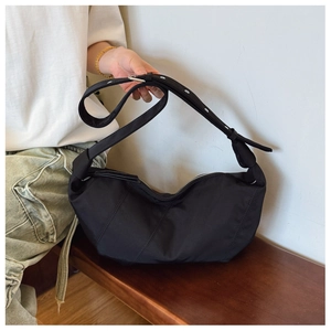 Detail of black pleated crescent bag featuring wide adjustable strap and silver eyelets