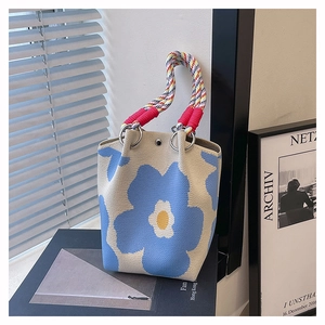Artistiek detail van een beige gebreide emmertas met blauw bloemenpatroon op boeken