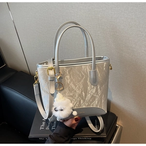 Détail du sac seau argenté plissé avec breloque peluche sur support de livre