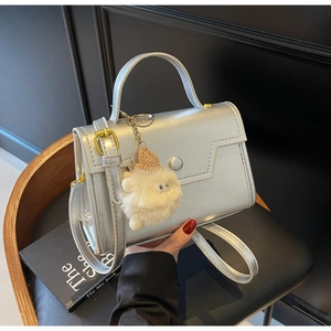 Dettaglio della borsa a tracolla argento con cuciture geometriche e ciondolo peluche
