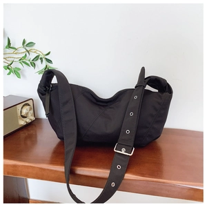 Detail of black crescent bag featuring quilted twill texture and metal eyelet wide strap