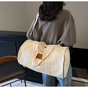 Detail of canvas travel bag featuring leather trim, brand tag, and side pocket detail